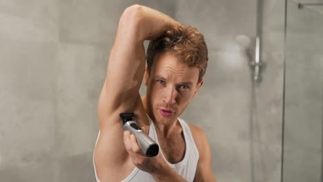 athletic man in a t-shirt shaves his armpits with an electric razor