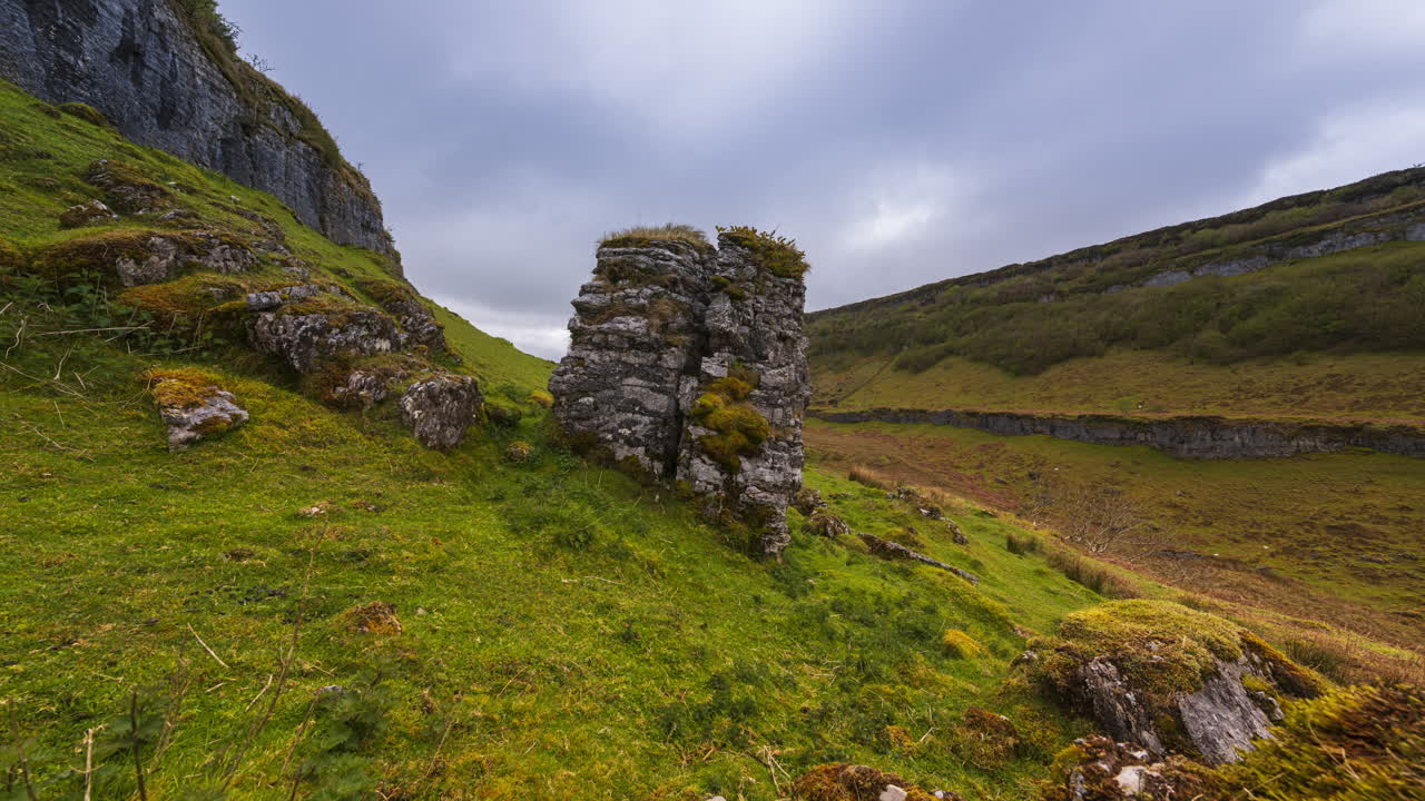 시골 풍경의 파노라마 모션 타임 스: 전면의 바위, 풀, 먼 계곡의 양, 구름이 많은 날, 아일랜드의 슬라이고 카운티의 카로킬에서 볼 수 있습니다.