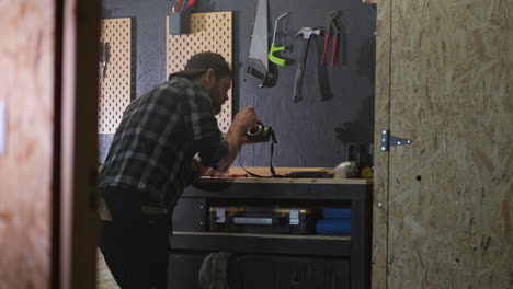 adult man repairs camera in workshop, equipment hang on black wall, dolly revealing shot