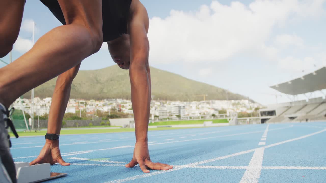 vista lateral de un atleta de raza mixta preparándose para una carrera en el estadio