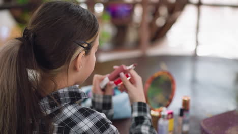 vista trasera de una mujer joven con el cabello atado y la camisa a cuadros observando de cerca los productos de belleza en la mesa de madera, la iluminación suave y el entorno natural mejoran la rutina de belleza y el tema de la organización cosmética