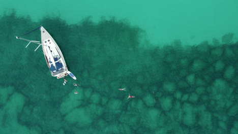 aerial view of people swimming towards the sailboat near playa del trench in mallorca, spain