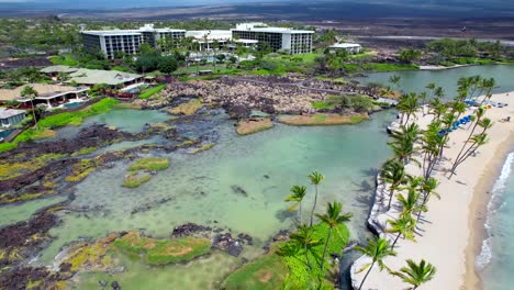 tidal pools and palm trees along a narrow sandy beach with hotels and resorts in the background - descending aerial view