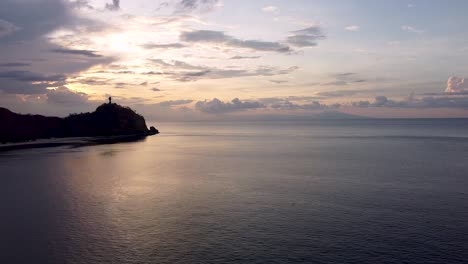 Statische-Drohnenaufnahme-Aus-Der-Luft-Auf-Wunderschöne-Wellen-über-Dem-Meer-Bei-Sonnenuntergang-Mit-Dem-Berühmten-Wahrzeichen-Von-Cristo-Rei,-Der-Jesus-Christus-Statue-In-Der-Ferne