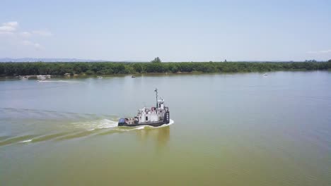 Old-rusty-boat-travels-on-river-in-Brazil,-slow-aerial-zoom-out-revealing-landscape