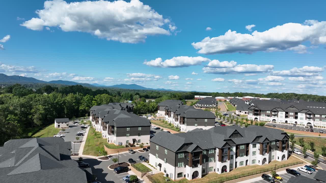 Aerial view of modern American apartment complex with uniform architecture, parking lots, and scenic mountain backdrop on a sunny day