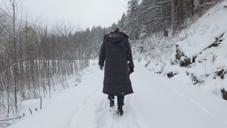 woman walking in the snow through the forest during snowfall in winter