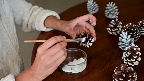 female hands tie the rope of a gift box with wrapping decorated with a pine branch and snowflakes