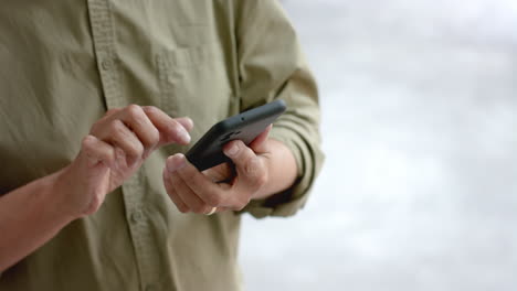 Midsection-of-senior-biracial-man-using-smartphone-standing-by-window-at-home,-slow-motion