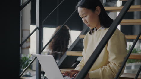 young woman working on a laptop on the stairs in an office.