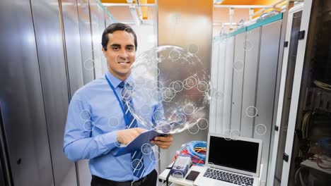 Animation-of-globe-with-icons-over-smiling-biracial-male-worker-inspecting-server-room