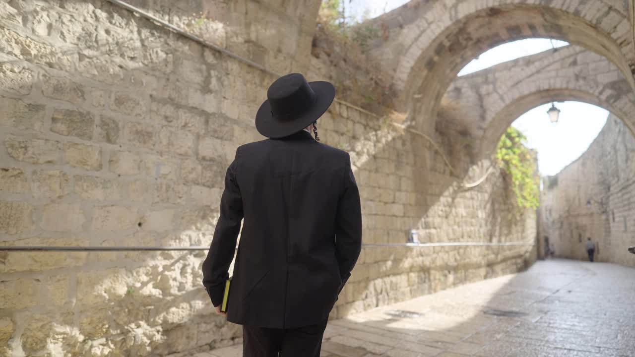 Orthodox Jewish Man With Book Walking Through Historical Western Wall In Jerusalem. slow motion, rear view