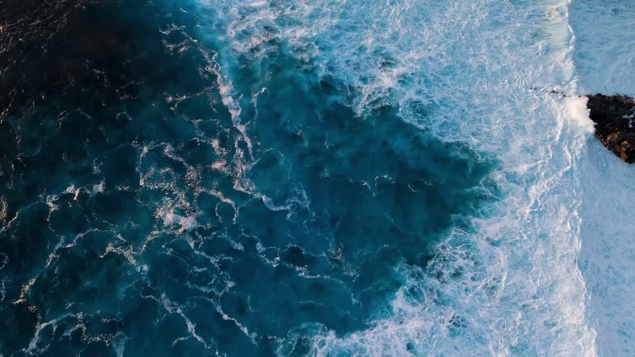 Beautiful drone footage of deep blue Atlantic waves crashing against rugged volcanic rocks at sunset in Lanzarote, Canary Islands, Spain.