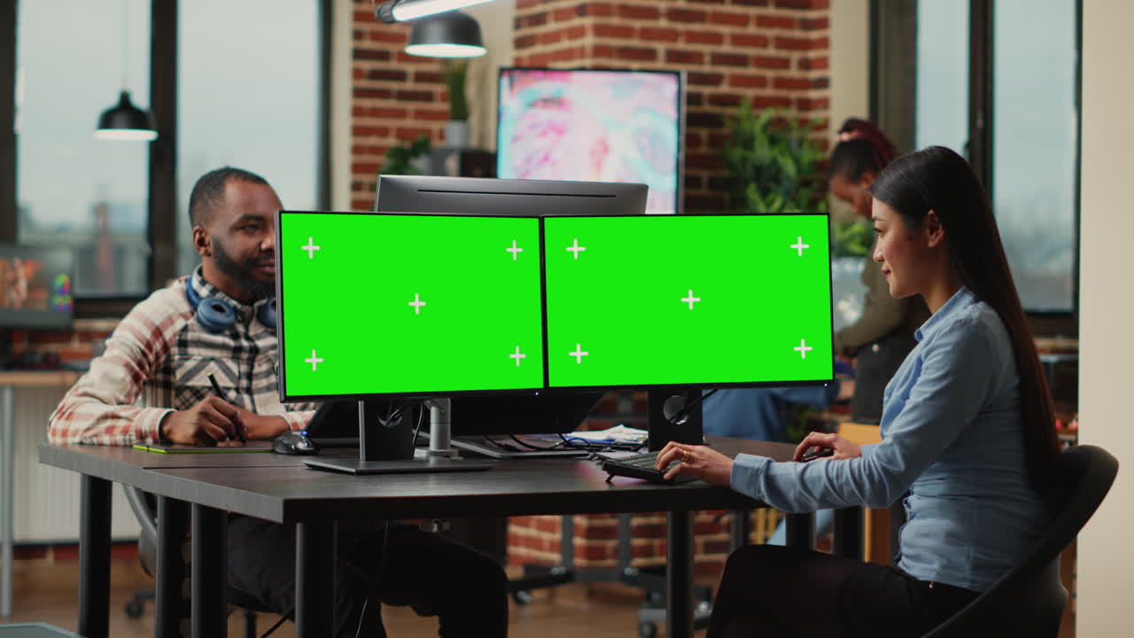 Asian digital editor looking at greenscreen on multiple monitors