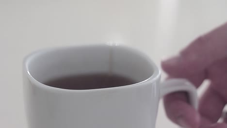 man do some tea in a morning before he go to work! the cup stands on a desk and he put the tea bag in a cup! then he pours the cup with a boiled water and waiting for tea been done!