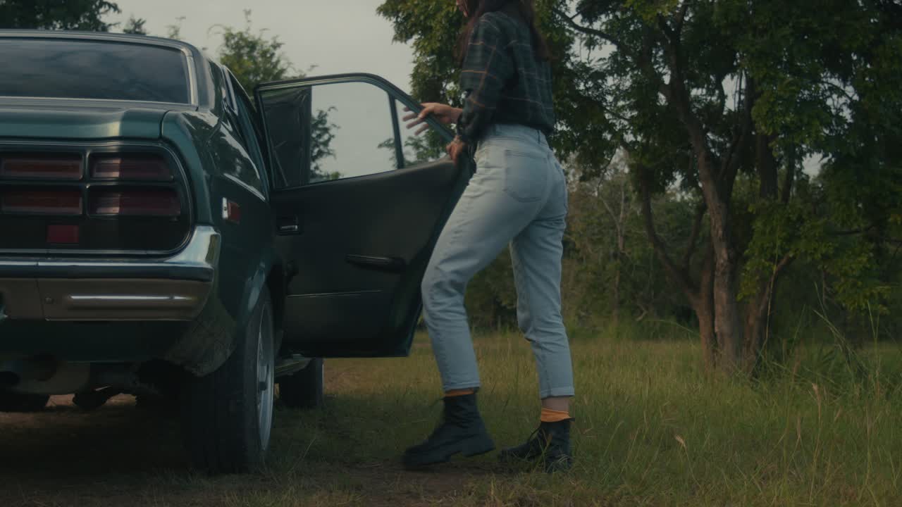 Donna accanto a un'auto d'epoca in un campo rurale