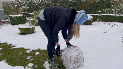 young woman rolling snow for snowball in garden building a snowman during winter