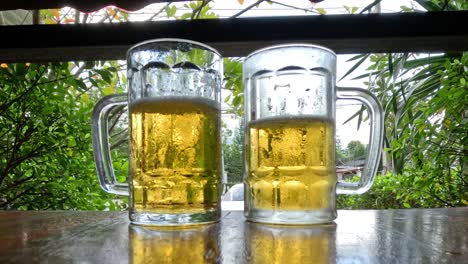 two beer mugs on a wooden table outside.