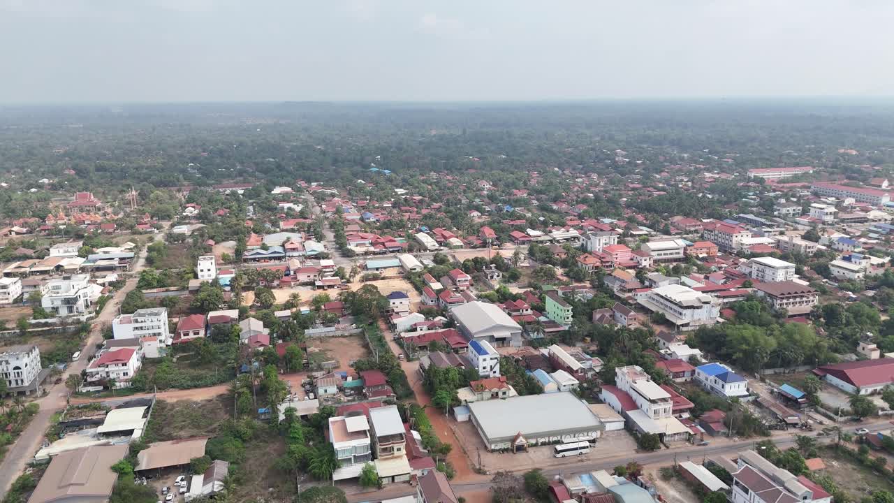In the distance, dense forest or undeveloped land dominates the horizon, suggesting the town is situated close to natural areas. The view, under an overcast sky