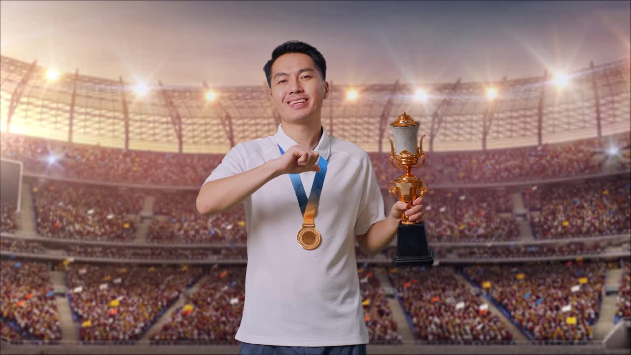 금메달을  아시아인 남자가 카메라에 금 트로피를 보여 주고, 스타디움에서 첫 번째 우승자로서 자랑스럽게 승리하고 있습니다.