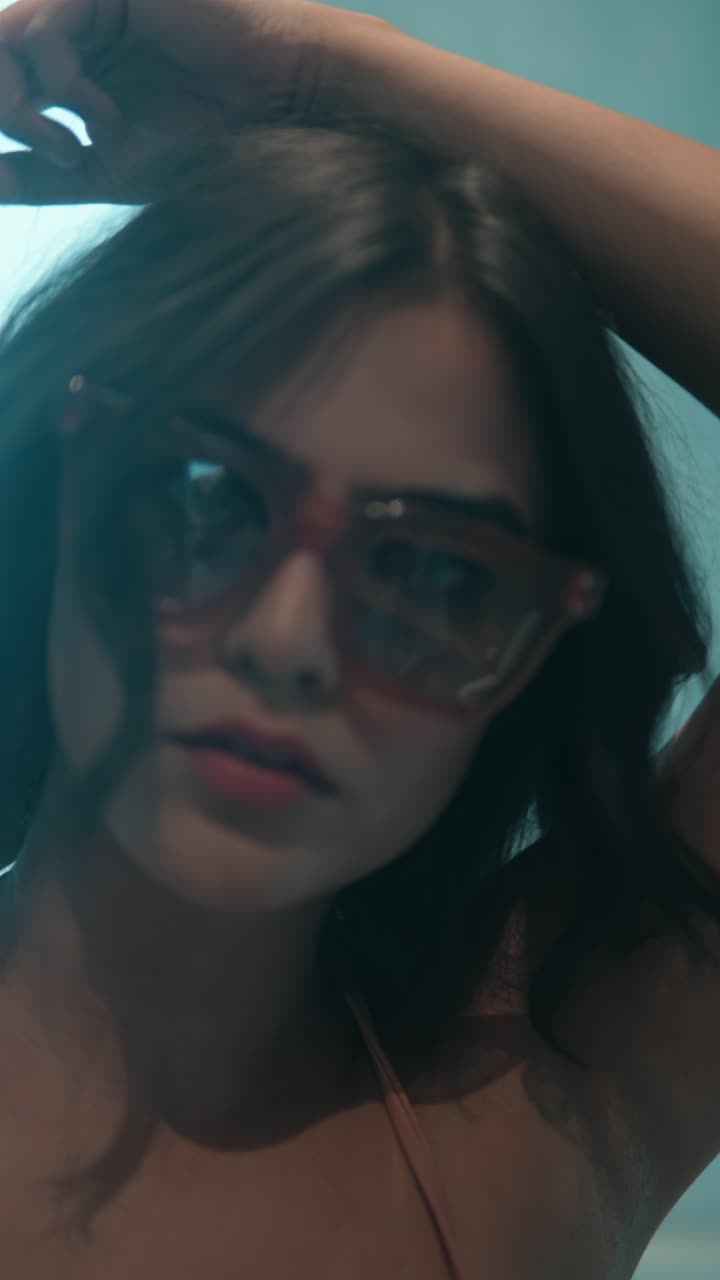 Stylish woman in sunglasses posing indoors with hand in hair, soft light and blur