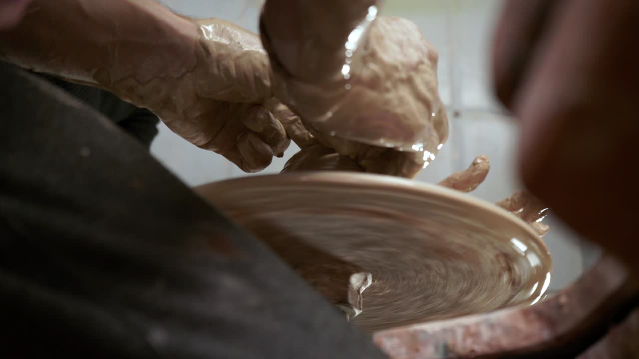 A potter teaches a woman to make clay dishes. A man takes a woman's hands