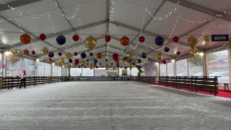 Niña-Patinando-Sobre-Hielo-Sola-En-Una-Pista-De-Hielo-Cubierta-Desierta-Con-Adornos-Navideños-En-El-Techo