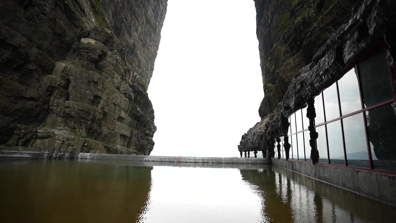 Malerischer Stausee am Tianmen Berg mit einem Betonstaudamm und Gehweg, die sich im ruhigen Wasser spiegeln.
