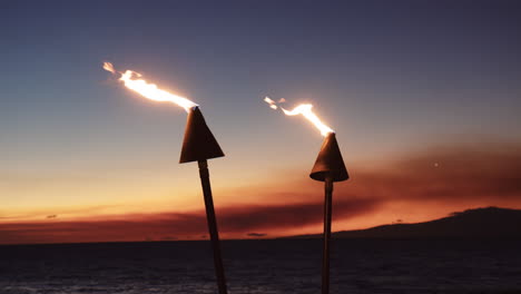 antorchas tiki contra el cielo del atardecer en la playa de wailea, maui, hawaii