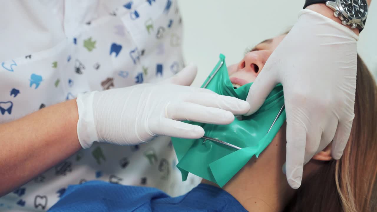 A dentist in white latex gloves makes a green rubber dam with a metal frame. Beginning of a treatment procedure in a dental clinic
