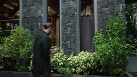 man interacts with a device outside a modern building surrounded by plants