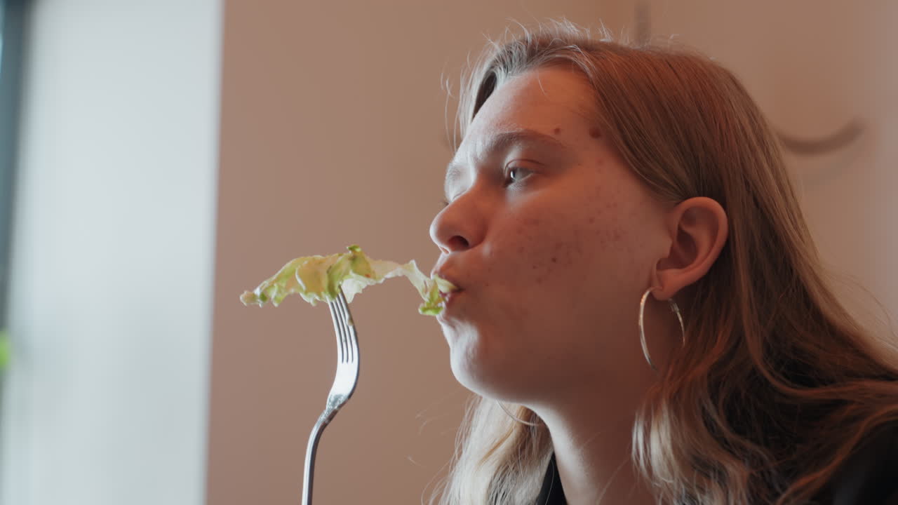 Signora contemplativa che annusa la vegetazione. Scena di caffè interno con donna pensierosa e fogliame verde. Donna con lentiggini e orecchini a cerchio si diletta ad annusare le foglie in un ambiente accogliente di caffè.