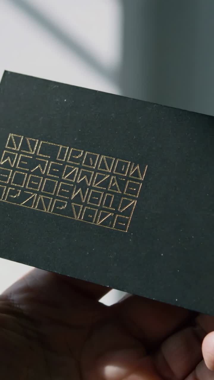 Vertical video: Catching sun, hand rotating and tilting black card at window, showing foil symbols