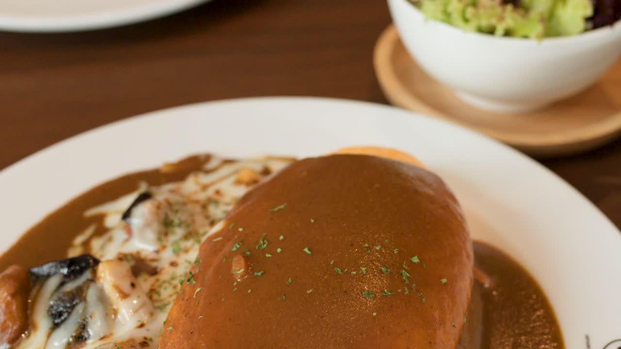 Close-up pan of Japanese omelette rice, creamy sauce, salad, and soup in restaurant lighting