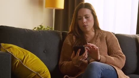 Puzzled-Woman-Sitting-On-Sofa-At-Home-Answering-Cold-Call-On-Mobile-Phone-That-She-Doesn't-Recognise-2