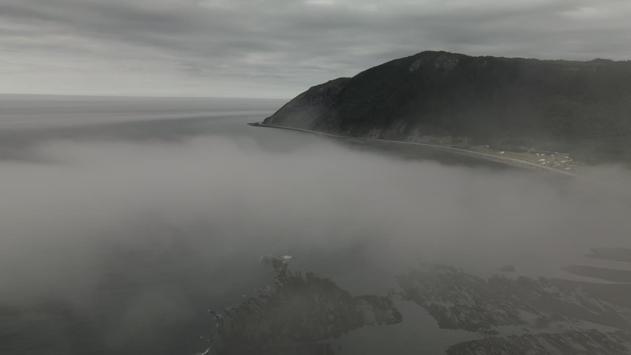 épica antena de drones volando a través de la niebla en un día nublado que revela montañas y la costa del océano atlántico de chic-chocs villlage, gaspesie