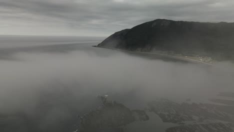 epic drone aerial flying through fog on overcast day revealing mountains and atlantic ocean coastline of chic-chocs villlage, gaspesie