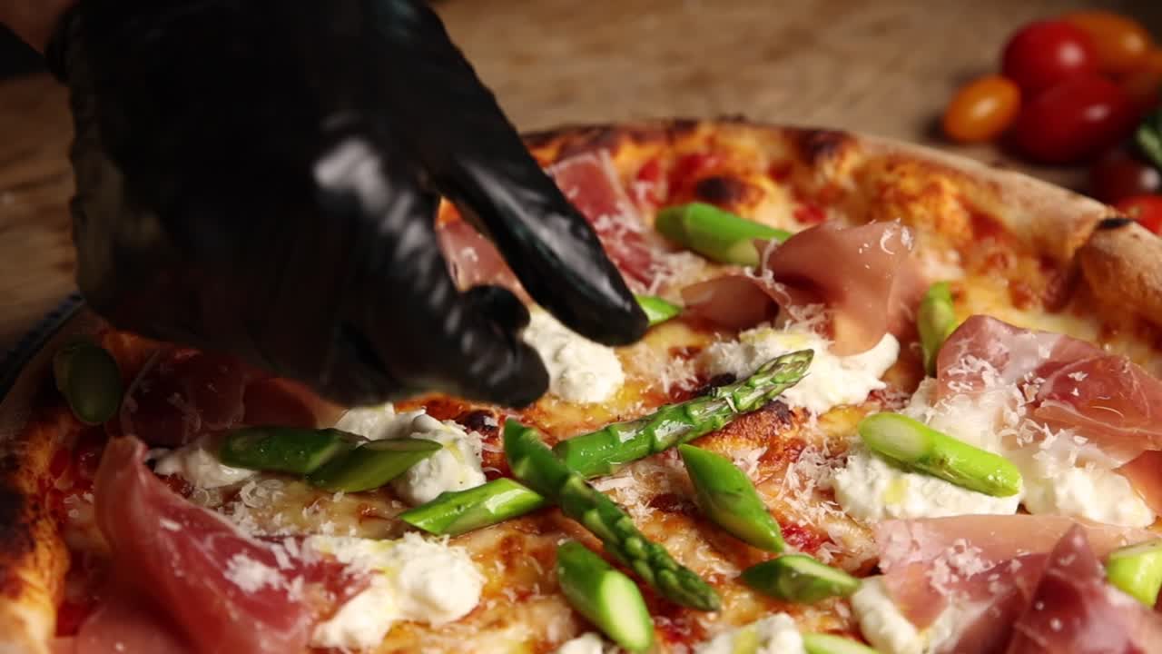 Chef's Hands in Gloves Placing Fresh Asparagus on Gourmet Pizza