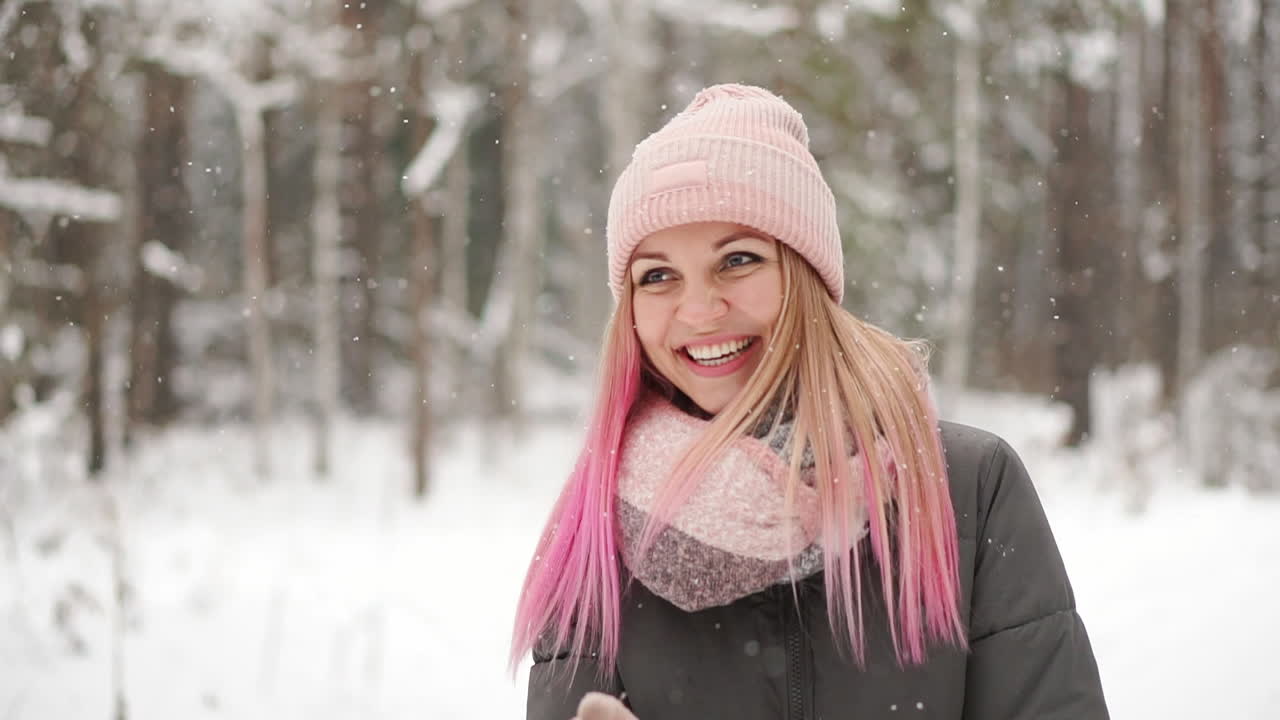 Rallentatore, donna d'inverno nel bosco che guarda la neve cadere e sorride guardando il cielo e direttamente nella telecamera