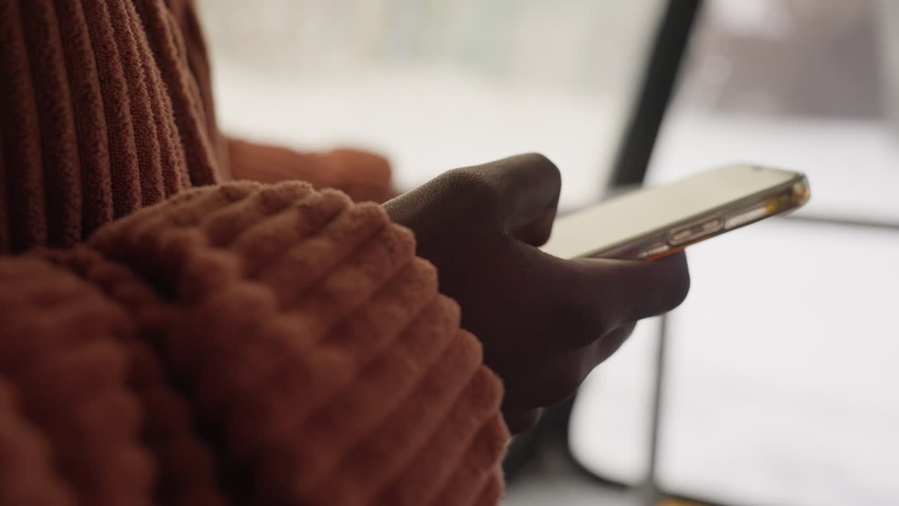 Un individuo si rilassa con il telefono durante una giornata nevosa. Una persona trova conforto in attività tranquille in una giornata gelida. Una persona si rilassa con il telefono accanto a una finestra coperta di neve durante il clima invernale.