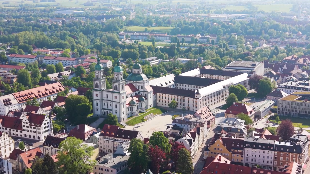 Detaljeret indzoomende droneoptagelse af Kempten i Bayern med Sankt Laurentius Basilikaen omgivet af historiske bygninger og et grønt bylandskab i klart dagslys, UHD.