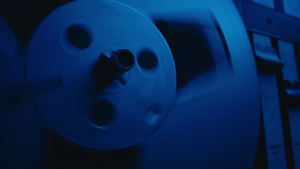 A vintage tape recorder spinning spools in a blue light