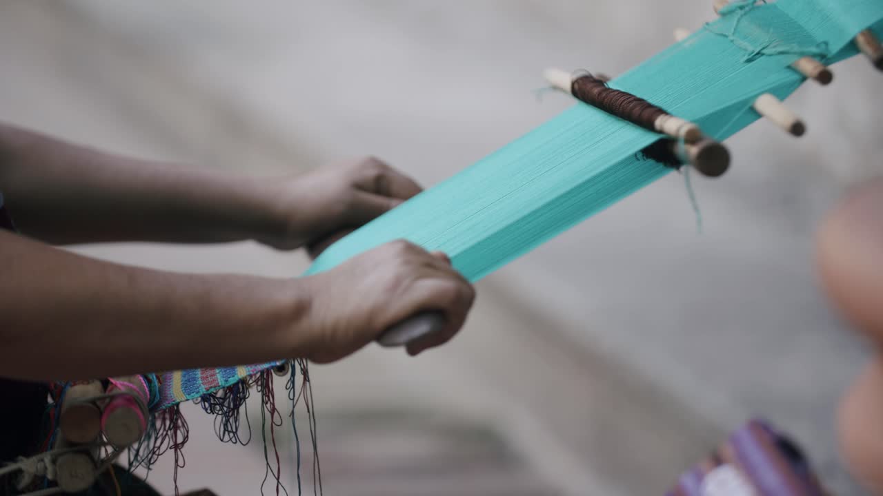imágenes en cámara lenta de una mujer indígena deslizando una regla de madera a través de hilos para hacer textiles únicos