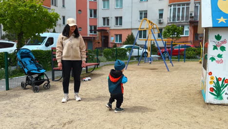 little toddler is on the playground with his mom. baby boy plays with a ball outdoors.