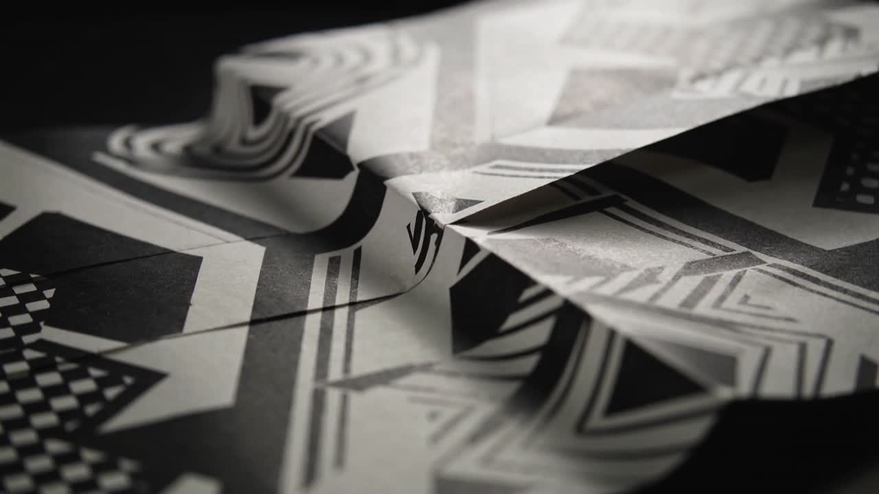 Carta geometrica che reagisce al tiro di messa a fuoco e alla luce dello studio, piegandosi in un lembo triangolare per il design.