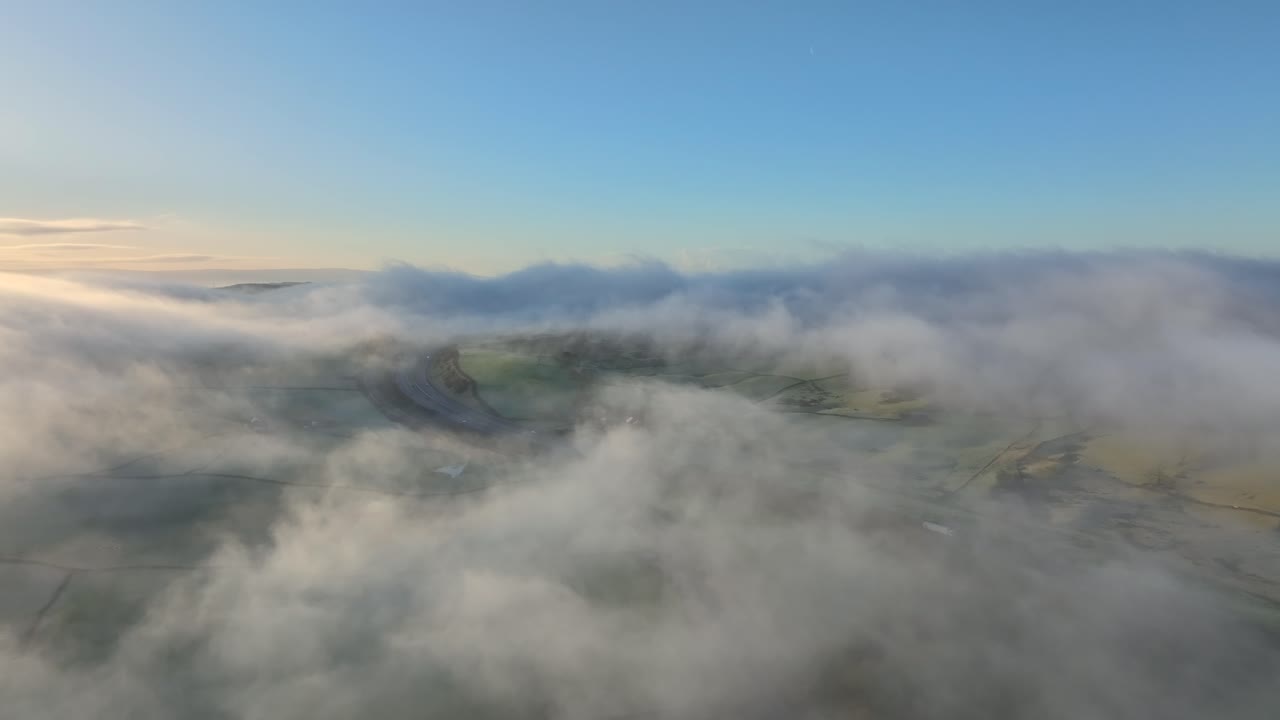 volando por encima de nubes bajas y niebla cerca de la autopista m6 hacia campos de tierras de cultivo de patchwork al amanecer en invierno