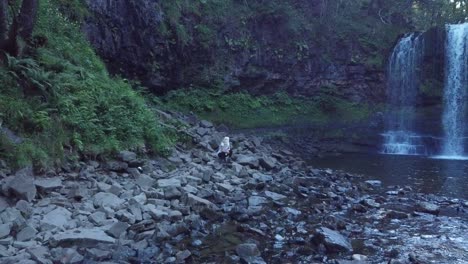 Girl-sitting-on-rocks-next-to-a-large-waterfall-in-Wales