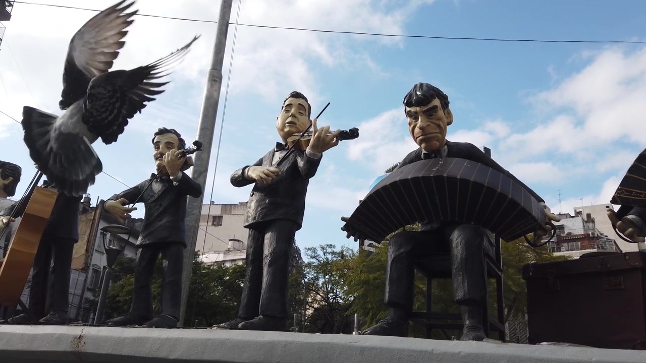 Vista panorámica en ángulo bajo de estatuas de músicos de la Orquesta de Tango Osvaldo Pugliese con edificios de la ciudad y una paloma en Buenos Aires, Argentina