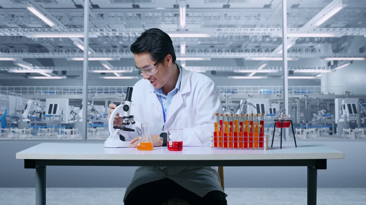 연구실에 앉아서 현미경으로 플을 분석하는 동안 미소 짓고 와우라고 말하는 실험관 위에 있는 현미경을 통해 보는 아시아인 과학자