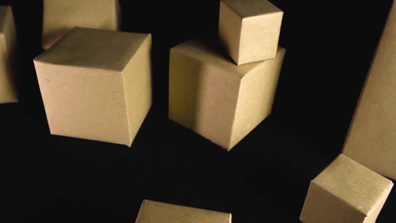Slow camera movement passing over several brown cardboard boxes of various sizes, representing concepts of shipping, packaging, and logistics on a simple dark, seamless background